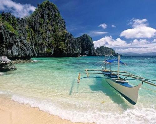Playa de arena blanca con un bote tradicional en El Nido